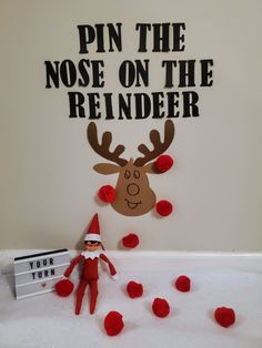 an elf with red pom poms is next to a sign that says pin the nose on the reindeer