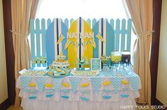 a table topped with cake and desserts next to a window covered in blue and yellow curtains