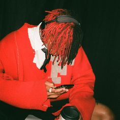 a man with dreadlocks is looking at his cell phone while wearing a red sweater