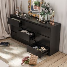 a black dresser with drawers in front of a mirror and flowers on the floor next to it