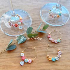 three wine glasses filled with different types of bead jewelry on top of a wooden table