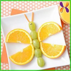 a plate with oranges, grapes and an insect made out of fruit on it