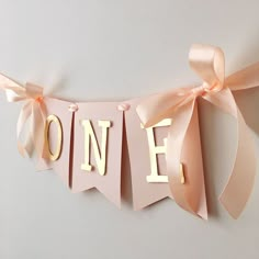 a pink banner with the word one hanging from it's side and ribbon on top