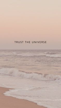 the words trust the universe are written in black on an ocean beach with waves crashing