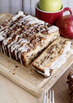 there is a piece of cake with icing on the cutting board next to an apple