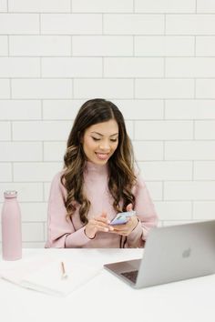 a woman sitting at a table with a laptop and cell phone in front of her