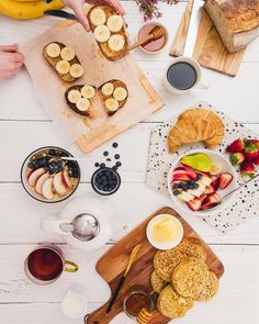 a table topped with fruit and pastries on top of a wooden cutting board next to other foods