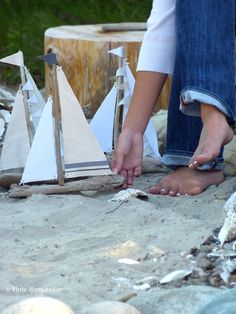 a woman is sanding on the beach next to small sailboats and logs,