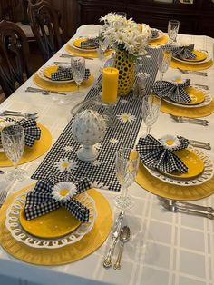 the table is set with yellow plates and black and white napkins, silverware, and flowers