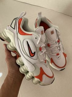 someone holding up a pair of white and orange sneakers