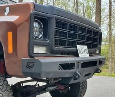 the front end of a brown truck parked in a parking lot next to some trees