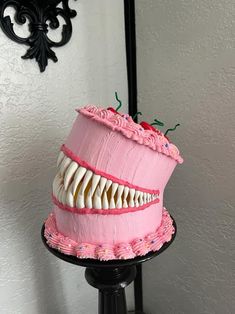 a pink cake with white teeth on a black stand in front of a gray wall