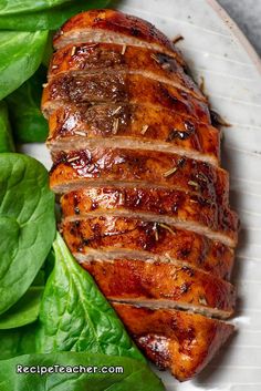 a white plate topped with meat next to spinach leaves on top of a table