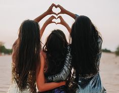 three girls are holding their hands in the shape of a heart while standing in water