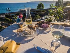 an outdoor table with plates and glasses on it, overlooking the ocean in the background