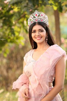 a beautiful young lady wearing a tiara and smiling at the camera with trees in the background