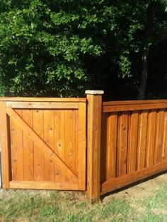 a wooden fence with a sliding gate in the middle of grass and trees behind it