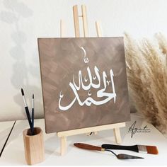 an easel with some paint and brushes on it next to a painting that has been written in arabic