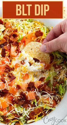 a hand dipping a tortilla chip into a bowl filled with shredded cheese and bacon