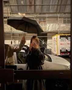 a woman holding an umbrella while standing next to a man in front of a car