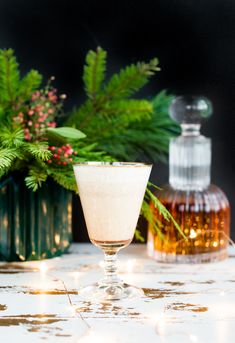 a glass filled with liquid sitting on top of a table next to bottles and plants