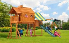 children playing on wooden playset with slide and swing set in grassy area, against blue sky