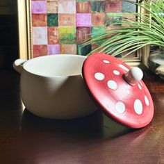 a red and white bowl sitting on top of a table next to a potted plant