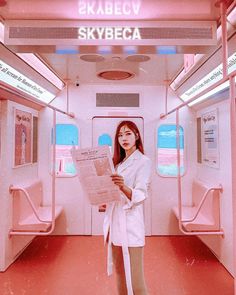 a woman is reading a paper while standing in a train car with the skybeca sign above her