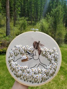 a person holding up a white embroidery art work with flowers in the shape of a woman's face