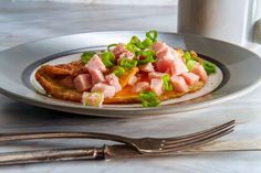 a plate with ham and green onions on it next to a fork, knife and cup