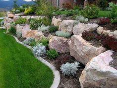 a large rock garden in front of a house with green grass and flowers on the side