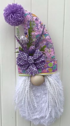 a purple and white gnome hat hanging on the side of a door with flowers in it