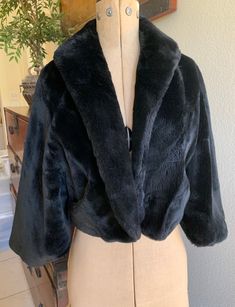 "Vintage genuine BORG Borgana black fur capelet jacket, short length, full shawl collar and dolman, untapered sleeves (see photos). Neiman Marcus Sports Shop label as well as label indicating a genuine BORGANA Borg fabric. Fully lined with beautiful shade of light peach satin. This is a short, just below the waist capelet with a \"blouson\" back and beautiful shawl collar. There are two small pockets on the front, just big enough for hands to stay warm. There is no size label, but here are the measurements. Overall length at back 22\" of fabric but 2\" is turned under for the blouson effect. Front length is 20\". Sleeve length from top of neck is 21\". Capelet is extra small and will fit size 0-2. Likely made in the 1940's. Fully lined. Excellent condition with no faults." Capelet Jacket, Fur Capelet, Sports Shops, Light Peach, Black Faux Fur, Size Label, Shawl Collar, Stay Warm, Neiman Marcus