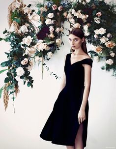 a woman in a black dress standing next to flowers