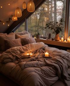 an unmade bed with candles on it in front of a window overlooking the woods