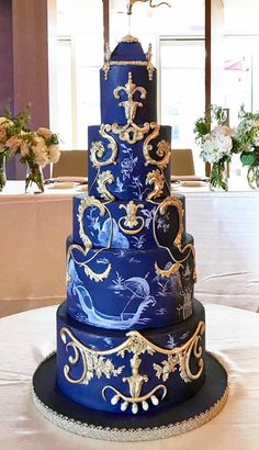 a three tiered blue and gold wedding cake sitting on top of a white table