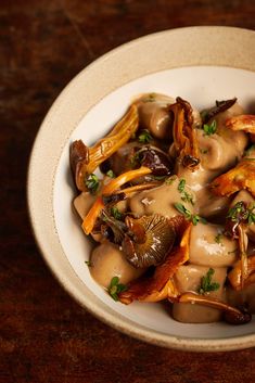 a white bowl filled with mushrooms covered in gravy on top of a wooden table