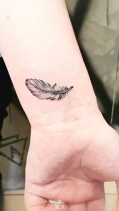 a small feather tattoo on the wrist is shown in black and grey ink, with an arrow