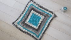 a crocheted square is laying on the floor next to a ball of yarn