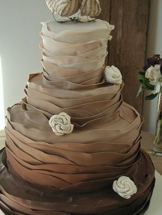 a three tiered chocolate cake with white flowers on the top and bottom, sitting on a table in front of a window