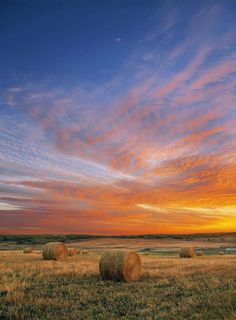 the sun is setting over hay bales in an open field with blue sky and clouds