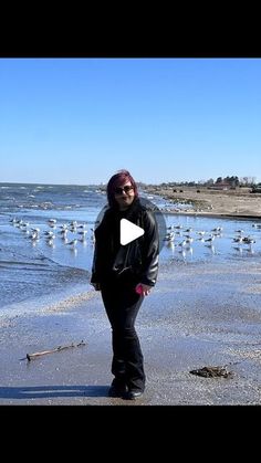 a woman standing on top of a sandy beach next to the ocean with seagulls