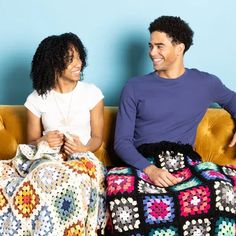 two people sitting on a couch with crocheted afghans in front of them