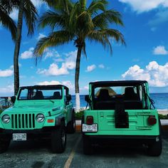 two green jeeps parked next to each other in front of palm trees and the ocean