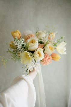 a woman holding a bouquet of flowers in her hand with white and yellow roses on it