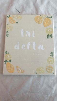 a canvas with the words tri deita written in white paint surrounded by lemons and oranges