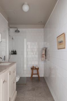 a white tiled bathroom with a stool in the corner