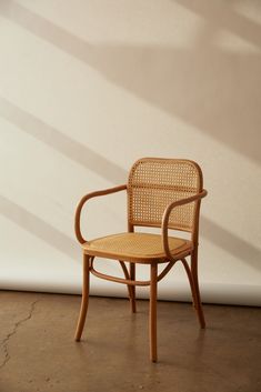 a wooden chair sitting in front of a white wall with shadows on the walls behind it