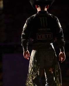 a man with a cowboy hat and long skirt standing in front of a dark background