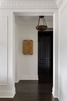 an empty hallway with white walls and wood floors, black door and light fixture hanging from the ceiling